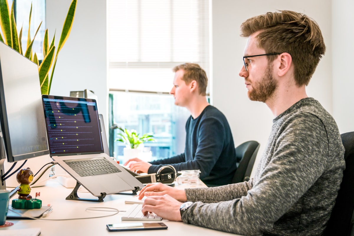 Deux professionnels de la sécurité informatique travaillant côte à côte devant leurs ordinateurs portables dans un bureau moderne